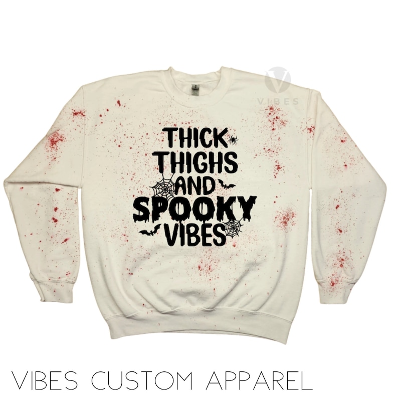 May include: White sweatshirt with red splatter paint and black text that reads "Thick Thighs and Spooky Vibes" with spiderwebs and bats.