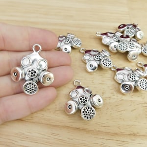 May include: A set of ten silver-toned gas mask charms. The charms are detailed and have a realistic look. They are perfect for adding a unique touch to jewelry or crafts.