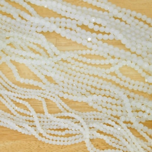May include: Multiple strands of white faceted glass beads, arranged in a loose pile on a wooden surface.
