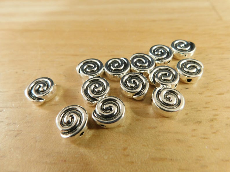 May include: A group of silver metal beads with a spiral design. The beads are scattered on a wooden surface.