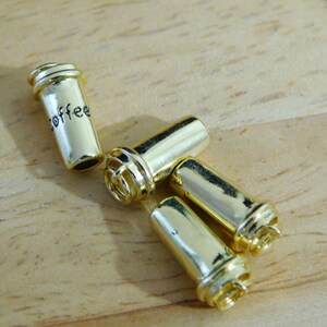May include: Four gold-colored metal charms shaped like coffee cups. One charm has the word "coffee" engraved on it.