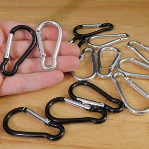May include: A group of silver and black metal carabiner clips. The clips are arranged in a circle on a wooden surface.