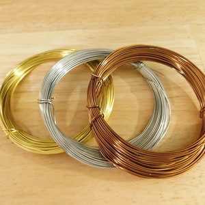 May include: Three spools of wire, one gold, one silver, and one copper, are arranged in a circle on a wooden surface.