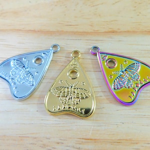 May include: Three silver, gold, and iridescent charm pendants shaped like a witch's board or planchette with a moth design.