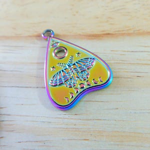 May include: A rainbow iridescent metal charm shaped like a witch's planchette with a moth design and crescent moons.