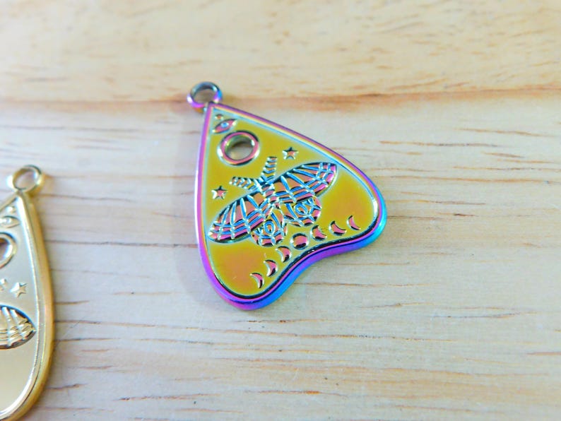 May include: A rainbow iridescent metal charm shaped like a witch's planchette with a moth design and crescent moons.