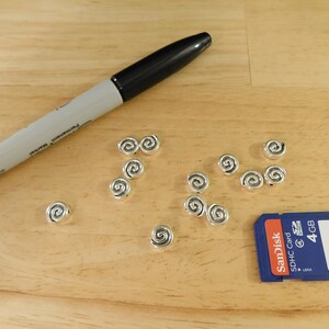 May include: A close-up of a wooden surface with a black marker and silver swirl beads. A blue and red SD card with the text "SanDisk sdhc card 4 GB" is also visible.