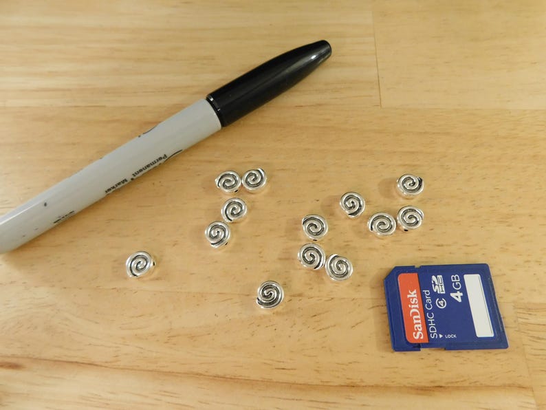 May include: A close-up of a wooden surface with a black marker and silver swirl beads. A blue and red SD card with the text "SanDisk sdhc card 4 GB" is also visible.