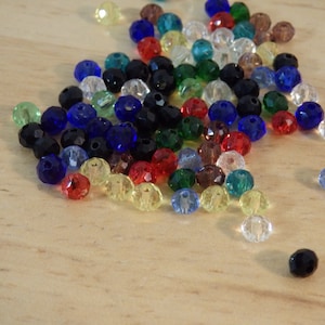 May include: A large assortment of colorful glass beads in various shades of blue, green, red, yellow, and clear. The beads are faceted and have a shiny finish.
