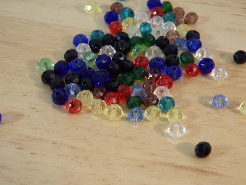May include: A large assortment of colorful glass beads in various shades of blue, green, red, yellow, and clear. The beads are faceted and have a shiny finish.