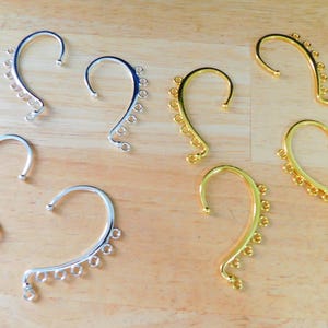 May include: Eight silver and gold ear cuffs with multiple decorative rings. The ear cuffs are designed to wrap around the ear and have a curved shape.