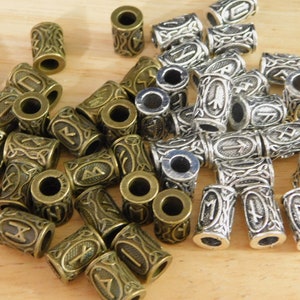 May include: A collection of silver and bronze metal beads with a rune symbol on each bead. The beads are cylindrical and have a hole in the center. The beads are arranged in a pile on a wooden surface.