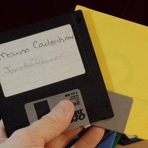 May include: Two floppy disks, one black with a white label that says "Melissa Cadenhead Jonathan Dhanor" and a yellow disk.