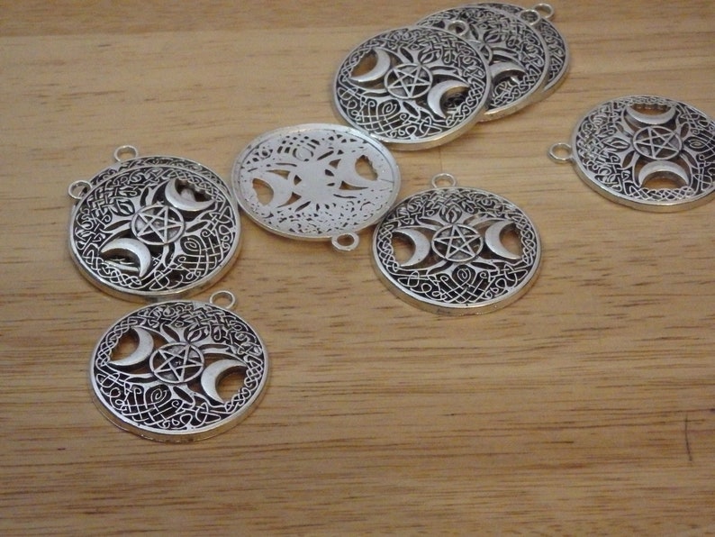 May include: A set of silver-toned metal charms featuring a triple moon and pentacle design. The charms are round and have intricate details.