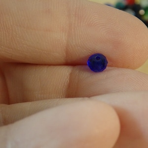 May include: A single, small, dark blue glass bead with a faceted surface.