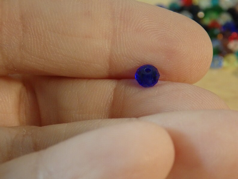 May include: A single, small, dark blue glass bead with a faceted surface.