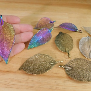 May include: Assortment of leaf-shaped metal charms in gold, silver, and iridescent colors. The charms have a delicate, textured design and are perfect for jewelry making or crafting.