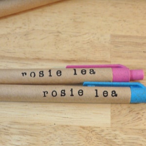 Op de afbeelding: Twee bruine kartonnen pennen met blauwe en roze dopjes. De pennen zijn gelabeld met "rosie lea".