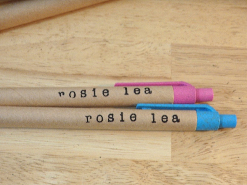 Op de afbeelding: Twee bruine kartonnen pennen met blauwe en roze dopjes. De pennen zijn gelabeld met "rosie lea".