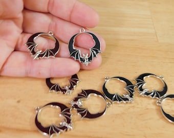 Può includere: Un set di sette ciondoli in metallo color argento con un pipistrello nero con le ali spiegate a forma di mezzaluna. I ciondoli hanno un foro nella parte superiore per essere attaccati a gioielli o altri oggetti artigianali.