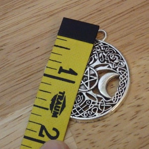 May include: Silver pendant with a tree of life design, a crescent moon, a pentagram, and Celtic knotwork. The pendant is 1 inch in diameter.