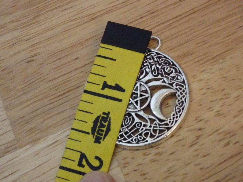 May include: Silver pendant with a tree of life design, a crescent moon, a pentagram, and Celtic knotwork. The pendant is 1 inch in diameter.