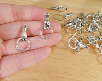 May include: Silver tone metal charms in the shape of a hand holding a ring. The charms are about 1 inch in size and have a detailed design.