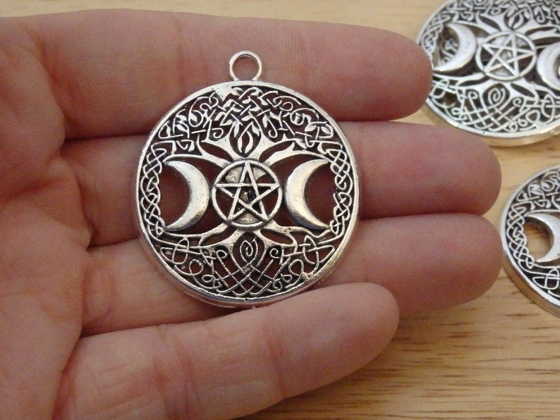 May include: Silver pendant featuring a tree of life design with three crescent moons and a pentagram. The pendant is intricately detailed and has a Celtic knot border.