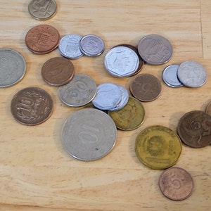 May include: A collection of coins from different countries, including silver, gold, and copper coins. The coins are arranged on a wooden surface.