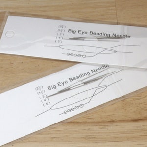 May include: Two packages of Big Eye Beading Needles. Each package contains a white card with a diagram of the needle and measurements in inches. The text "Big Eye Beading Needle" is printed on each card.