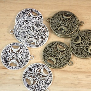 May include: A set of six metal charms featuring a triple moon and pentagram design. Three charms are silver and three are bronze.