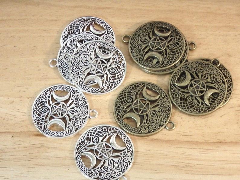 May include: A set of six metal charms featuring a triple moon and pentagram design. Three charms are silver and three are bronze.