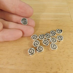 May include: A group of silver metal beads with a spiral design. The beads are about 1/2 inch in diameter.