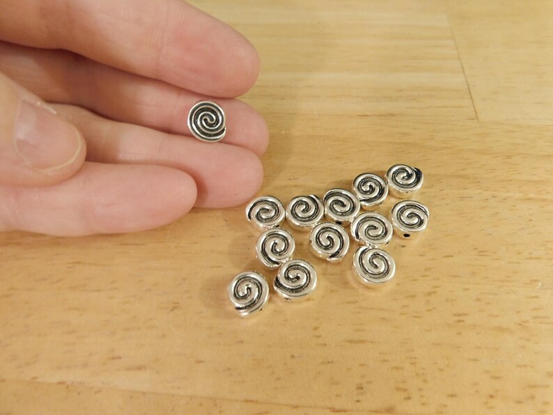 May include: A group of silver metal beads with a spiral design. The beads are about 1/2 inch in diameter.