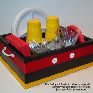 Puede incluir: Un organizador negro, rojo y amarillo con botones blancos y un asa. Contiene vasos amarillos, cubiertos de pl&aacute;stico transparente, servilletas rojas y un plato blanco. El organizador est&aacute; dise&ntilde;ado para cubiertos y utiliza latas de la tienda.