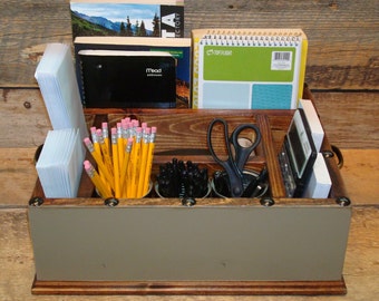 May include: A wooden desk organizer with multiple compartments. The organizer has a gray painted front and is filled with various office supplies, including pencils, pens, scissors, a calculator, and notebooks. The notebooks have the text "Top Flight" and "Mead" printed on their covers.