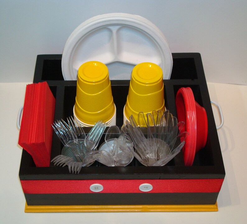 Puede incluir: Un organizador de madera negro y amarillo con compartimentos para vajilla desechable. Contiene vasos amarillos, tenedores y cuencos de pl&aacute;stico transparente, servilletas y platos rojos, y un plato blanco dividido. El organizador tiene una franja roja con botones blancos.