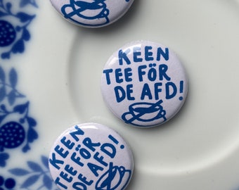 Könnte beinhalten: Drei weiße runde Knöpfe mit blauem Text und Illustrationen von Teetassen. Die Knöpfe sagen "Keen tee for de AFD!"