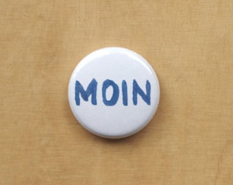 Pode incluir: Botão branco com a palavra "MOIN" escrita em azul.