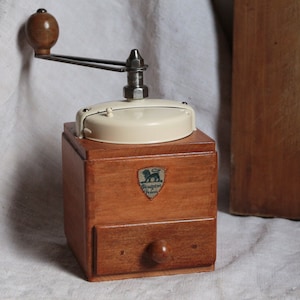 Antique french wooden coffee grinder with cream color metal top. French country kitchen. Rustic farmhouse decor. Manual coffee grinder