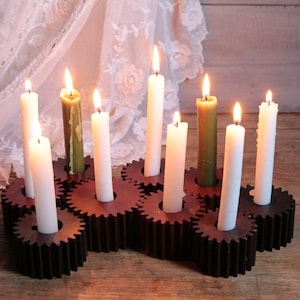 Könnte beinhalten: Ein Kerzenhalter aus Holz mit acht Kerzenplätzen in Form von Zahnrädern. Der Halter ist aus dunkelbraunem Holz und hat einen rustikalen Look. Die Kerzen sind weiß und grün.