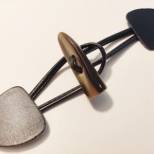 Könnte beinhalten: Ein brauner und schwarzer Toggle-Verschluss mit zwei Lederschlaufen. Eine Schlaufe ist dunkelblau und die andere ist schwarz.