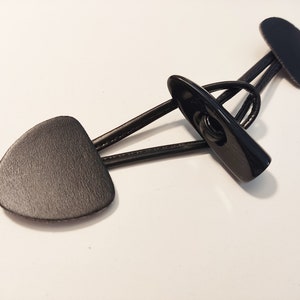 Könnte beinhalten: Schwarze Leder-Toggle-Verschluss mit zwei dreieckigen Teilen und einem schwarzen Metallverschluss.