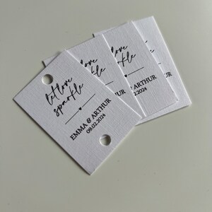 May include: White card stock tags with the text "Let love sparkle" and "Love like" in black script font. The tags also include the names "Emma & Arthur" and the date "09.02.2024" in black print.