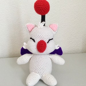 May include: White crocheted plush toy with purple wings, a red nose, and a red ball on top of its head.
