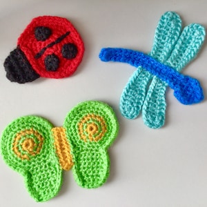 May include: Three crocheted felt ornaments: a red ladybug, a green butterfly with yellow accents, and a blue dragonfly.