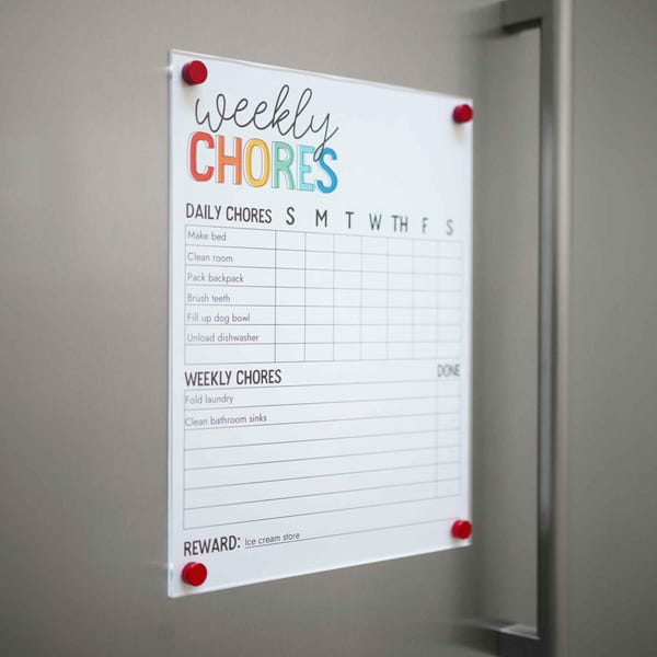 May include: A white dry-erase board with the words "weekly chores" in black script. The board is divided into daily and weekly chores with a grid for each day of the week. The board is attached to a refrigerator with red magnets.