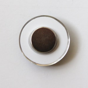 May include: A round white magnet with a silver rim and a brown magnetic center.