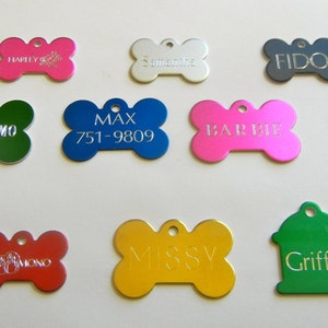 May include: A collection of 15 colorful metal dog tags in various shapes, including bone, heart, and fire hydrant designs. The tags are engraved with names, phone numbers, and other information.