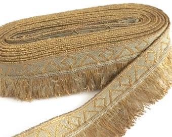 May include: A roll of gold and beige trim with a geometric pattern and fringe. The trim is approximately 1 inch wide.